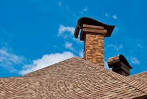 Two Chimneys with caps next to brown rood and blue sky background