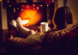 person sitting in a chair by a cozy fire with a hot beverage
