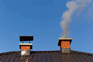 Two chimneys on a roof one has smoke billowing out