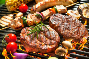 close up of a grill with burgers, vegetables and sausages on grill rods above a fire