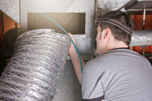 man cleaning air duct with light on head